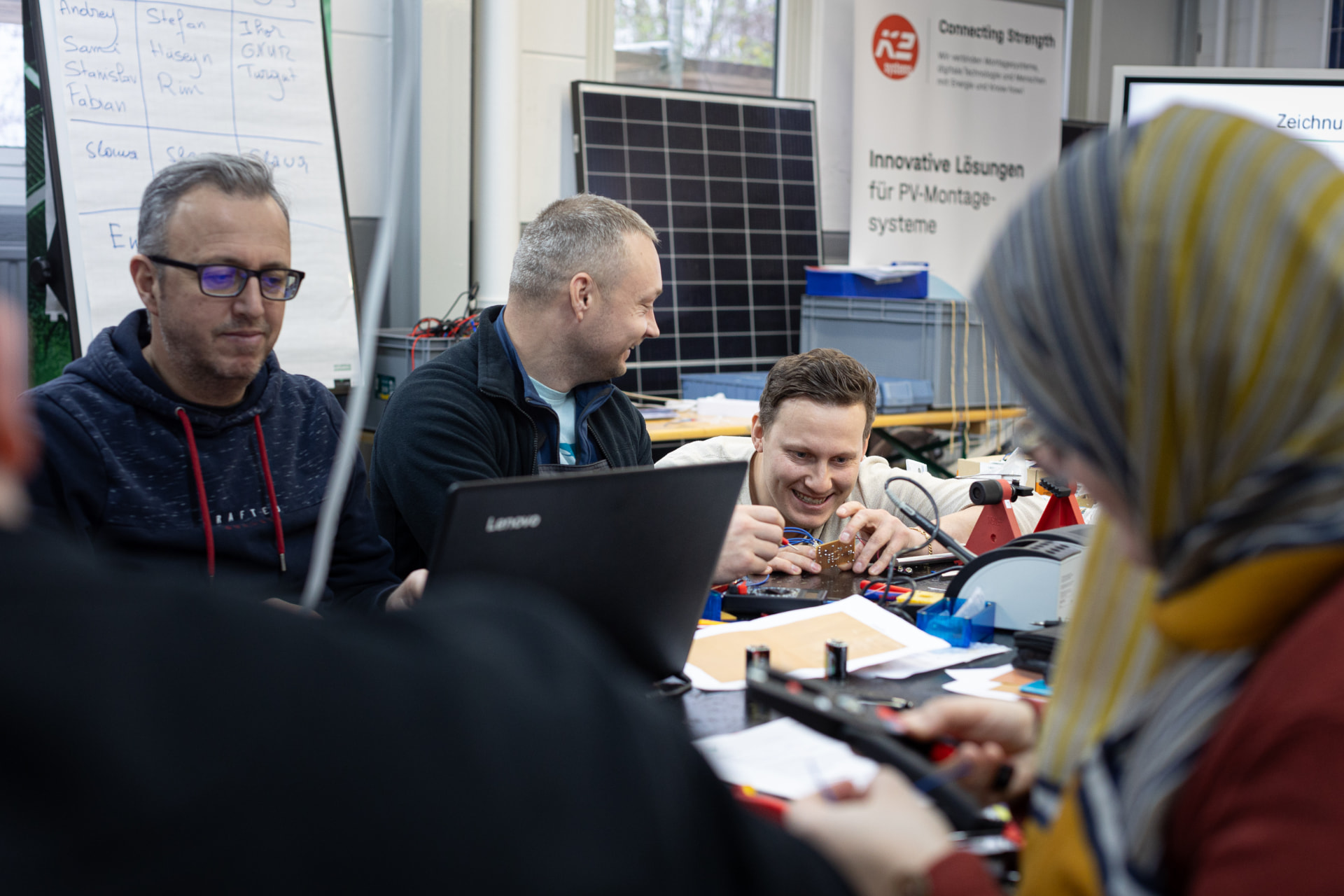 Teilnehmende arbeiten gemeinsam an elektronischen Bauteilen in einer Werkstatt mit Solarpanel